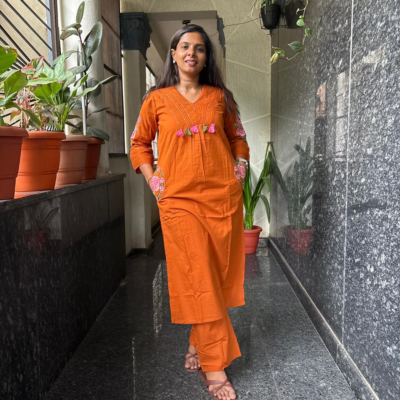 Close-up of V-neck pintuck and pink olive tassel detail on orange kurta